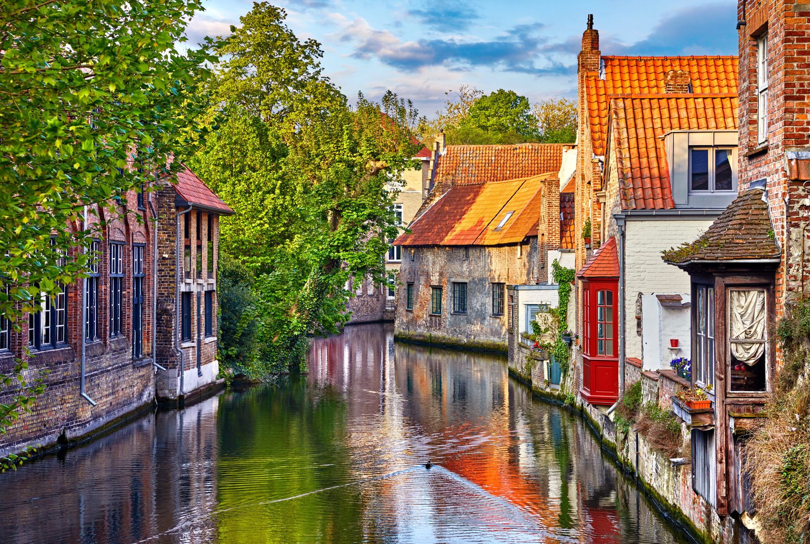 Brick houses and trees reflected in a quiet canal in Bruges